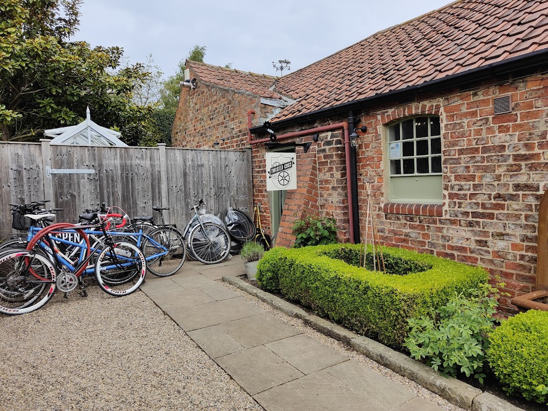 Bicycles parked outside a rustic brick building with a sign for "Twisted Cogs" and neatly trimmed hedges.
