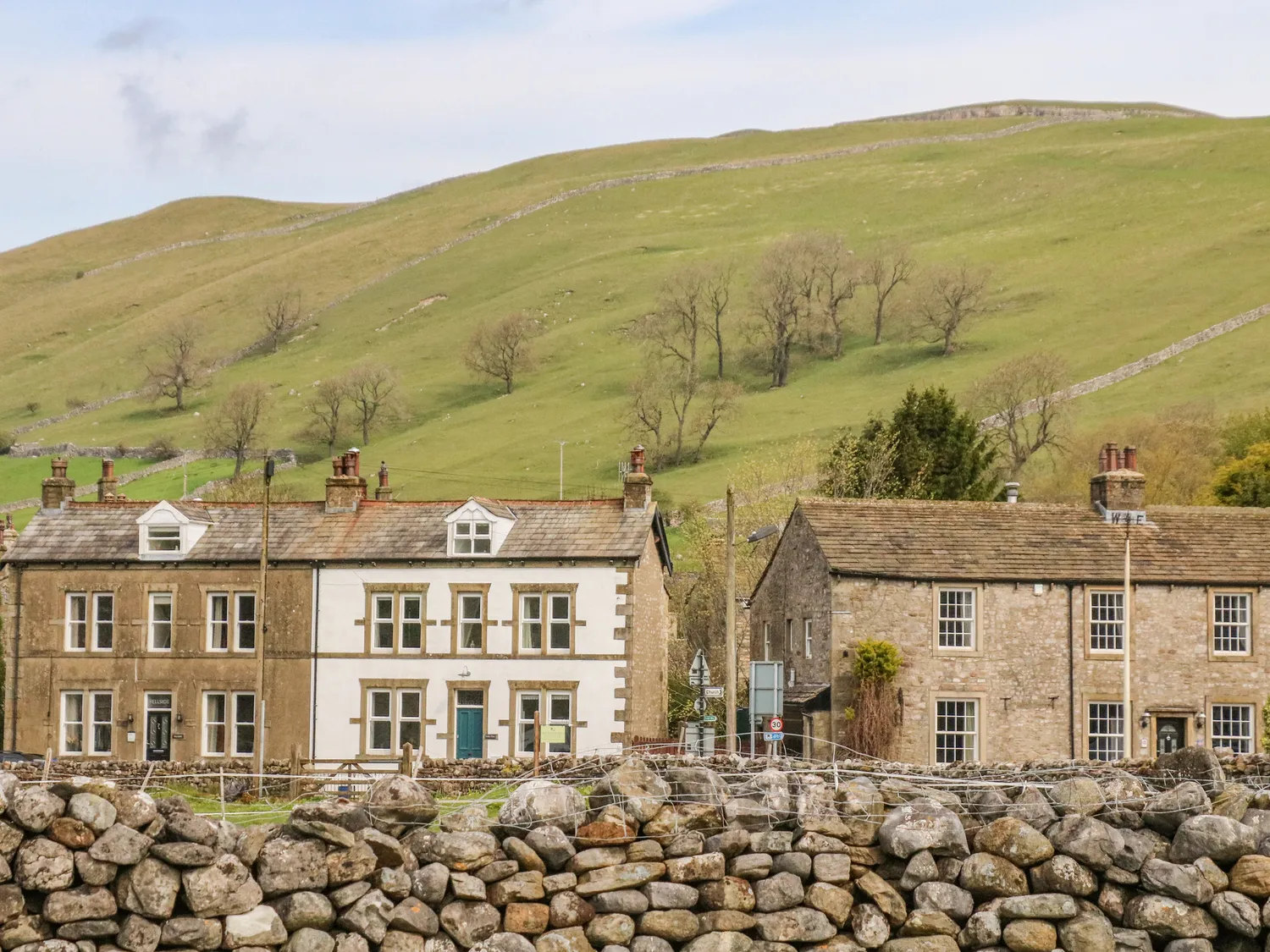 Stone cottages in Kettlewell, Yorkshire, with a rolling green hill and a stone wall in the foreground.