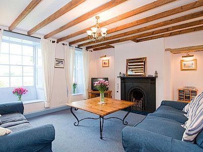Cozy Skipton cottage living room with exposed beams, blue sofas, floral decor, and a vintage fireplace.