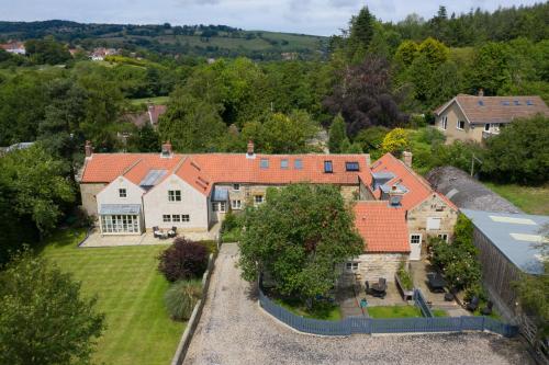 Drake Cottage in Whitby, surrounded by lush greenery and hills, features rustic stone buildings with red-tiled roofs.