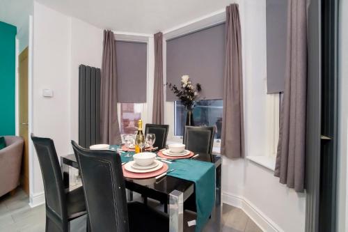 Dining area with set table, teal runner, black chairs, large windows with grey curtains, and vase with flowers in York.