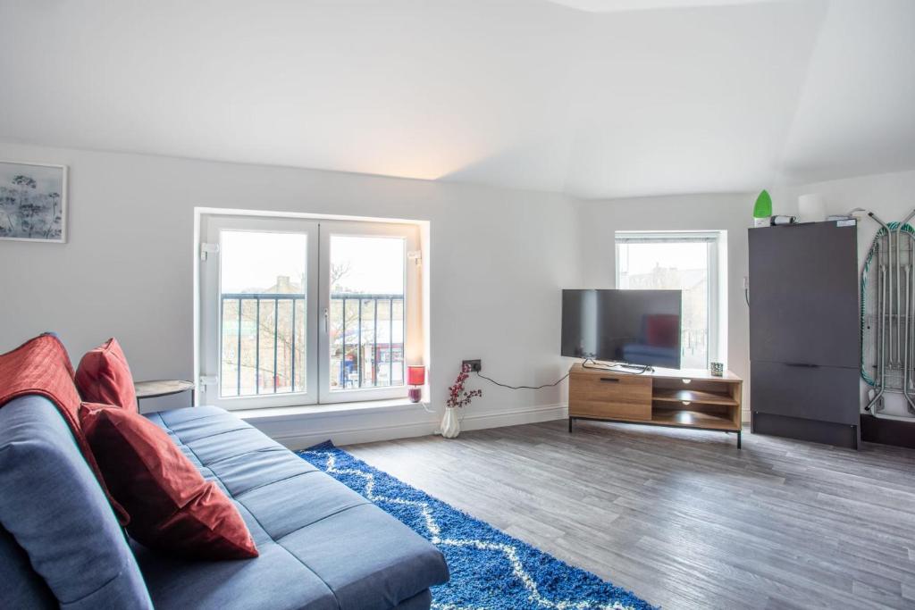 Modern living room in Bradford apartment, with blue sofa, red cushions, flat-screen TV, and large windows with views.