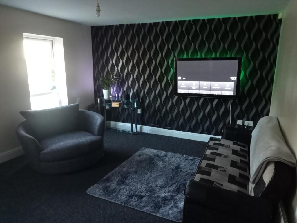 Spacious living room in Dudley Hill apartment, featuring modern decor, patterned wallpaper, plush seating, and a wall-mounted TV.