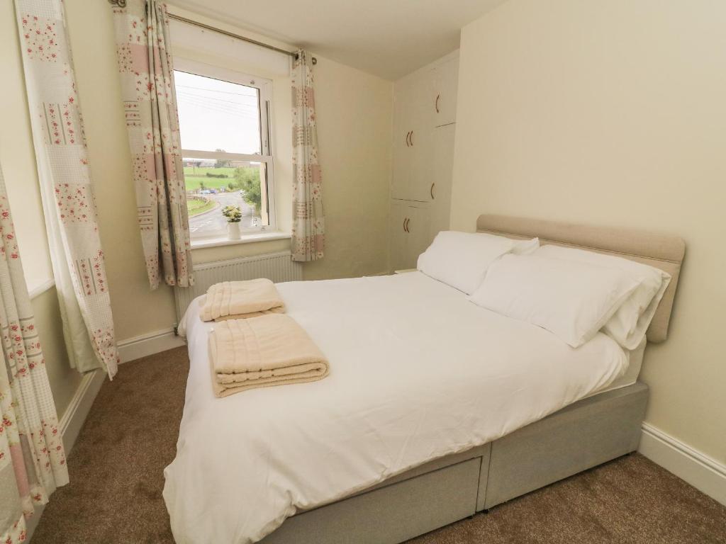 Cozy bedroom with a double bed, fluffy towels, floral curtains, and a window view of Aysgarth's green landscape.