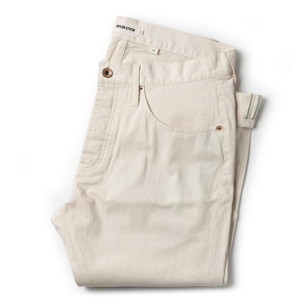 Natural organic selvage slim jeans in a light beige color, featuring a classic five-pocket design, subtle stitching, and a single green accent on the waistband.