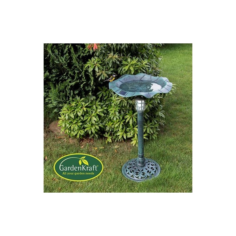 Green solar-lit outdoor bird bath with a decorative leaf design, made of durable material, featuring a sturdy pedestal and a solar light at the top, surrounded by lush greenery.