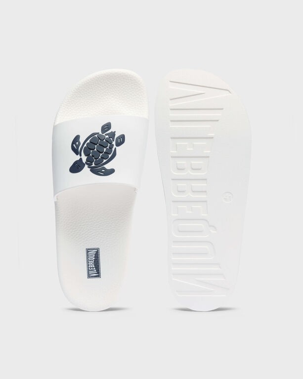 White beach slider sandals featuring a turtle graphic on the strap, made of durable material, with a textured sole and size 38 branding on the footbed.