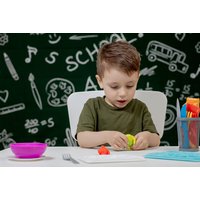 Child playing with colorful clay at a table, with school-themed doodles on a dark background.