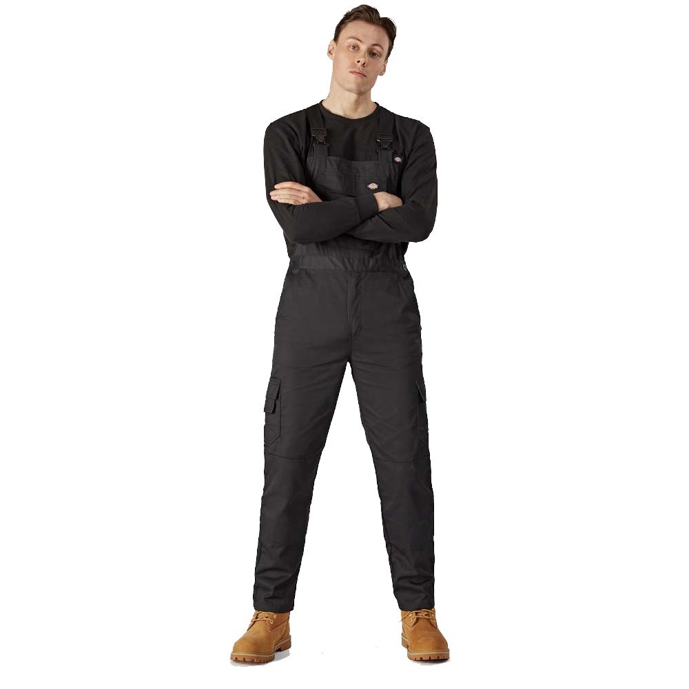 Black Dickies boiler suit with adjustable straps, side pockets, and a relaxed fit, worn over a long-sleeve black shirt, paired with tan work boots. Size: Medium.
