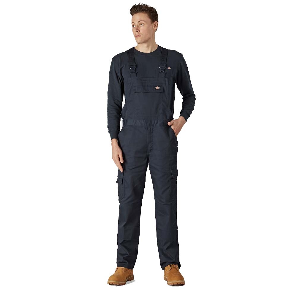 Navy blue Dickies boiler suit featuring adjustable straps, multiple pockets, and a relaxed fit, worn over a long-sleeve black shirt, paired with brown work boots.