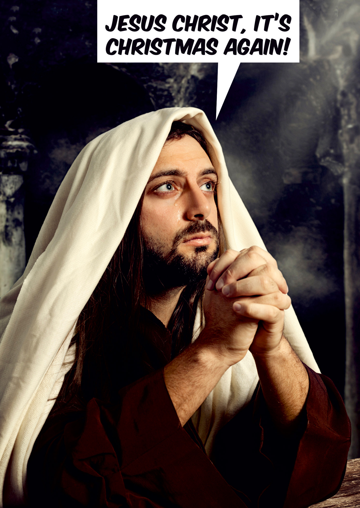 A man with long hair and a white robe, draped in a beige shawl, prays with a serious expression; text bubble reads "JESUS CHRIST, IT'S CHRISTMAS AGAIN!"