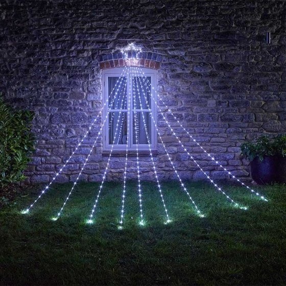 Cool white LED lights cascading in a shooting star design, with multiple strands extending from a central point, illuminating a stone wall and grassy area.