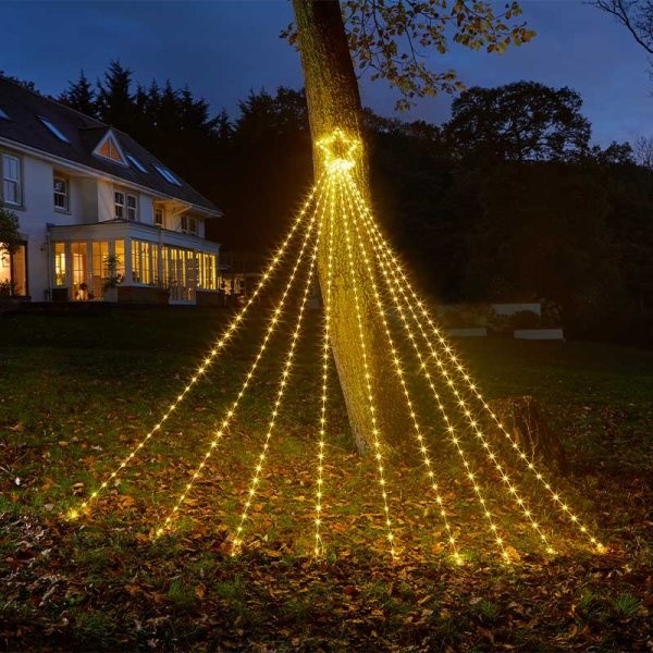 Warm white LED lights cascading from a tree in a shooting star design, creating a festive atmosphere in a garden setting with a house in the background.