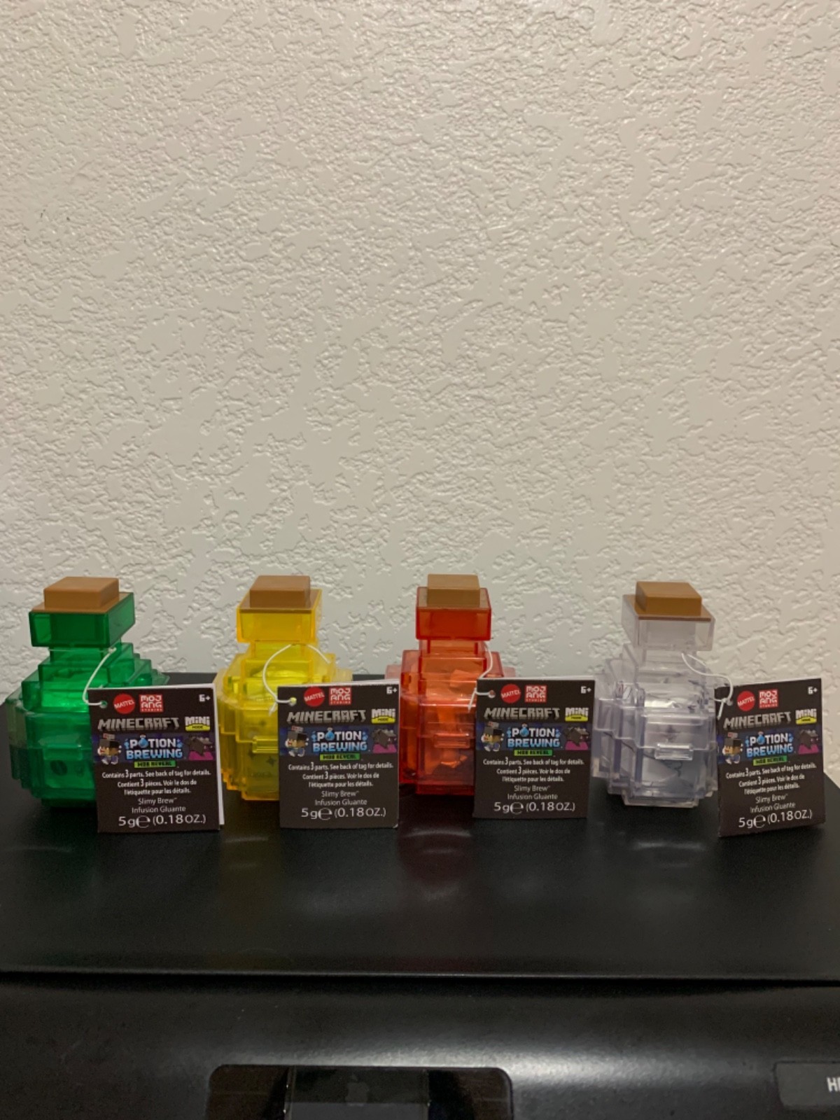 Five colorful potion figures from Minecraft, including green, yellow, red, and clear, each with a square brown lid and labeled with "Minecraft Potion Brewing" tags.