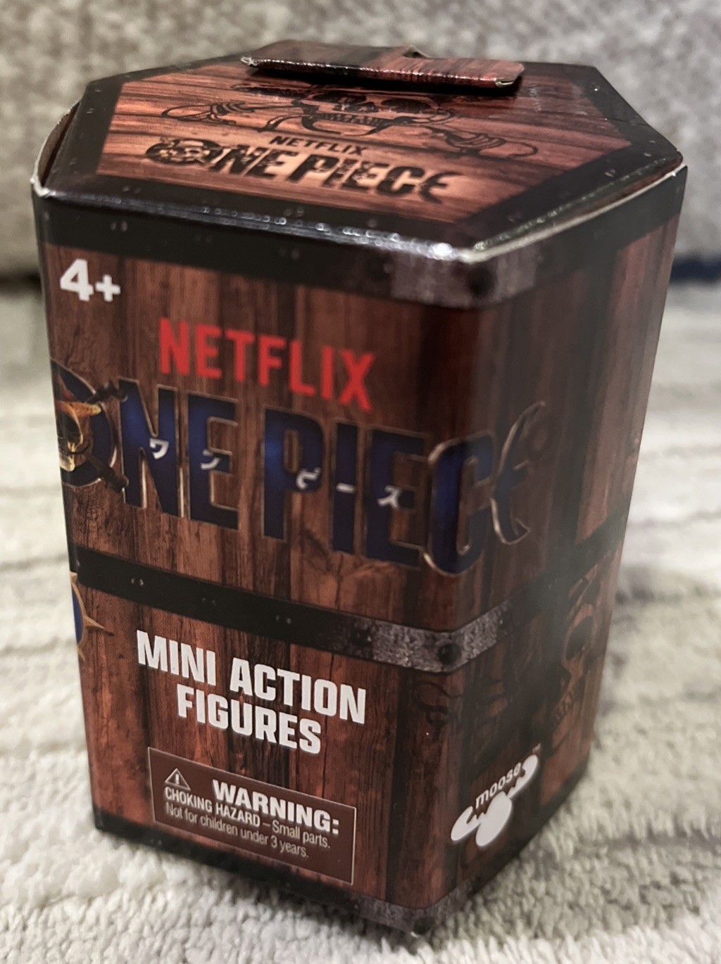 Hexagonal box featuring "Netflix One Piece Mini Action Figures" in bold lettering, with a wooden crate design and a warning label about small parts.