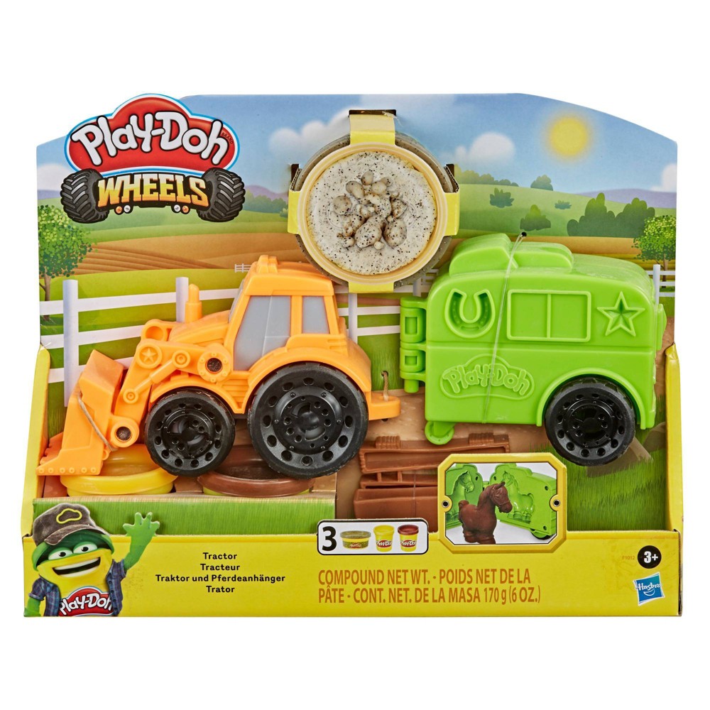 Bright orange tractor and green truck with black wheels, accompanied by a container of Play-Doh, set against a farm-themed background with a fence and grass.