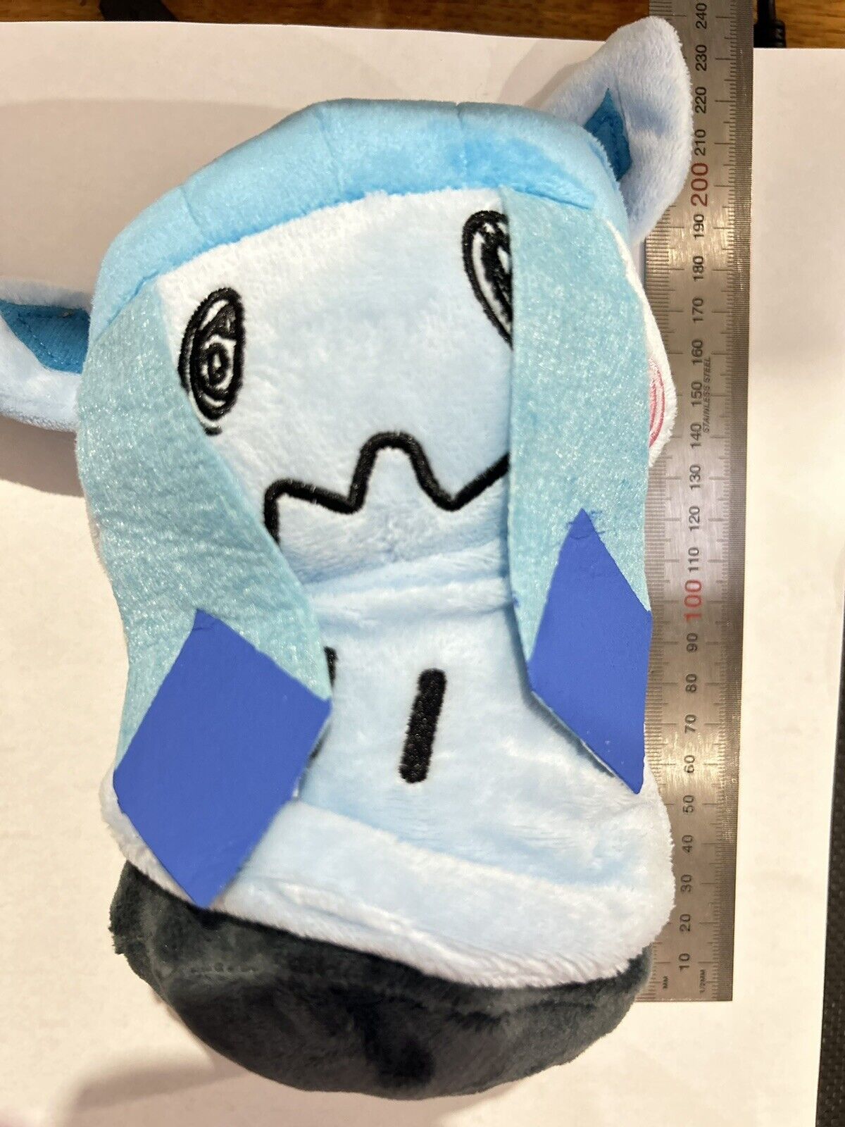 Soft toy of Mimikyu, featuring a blue and white plush body, large expressive eyes, and a black bottom, with a smooth, cuddly texture.
