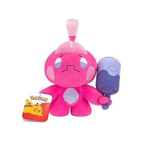 Pink Tinkatink soft toy with a round head, large eyes, and a purple hammer, made of plush material, accompanied by a Pokémon card featuring Pikachu.