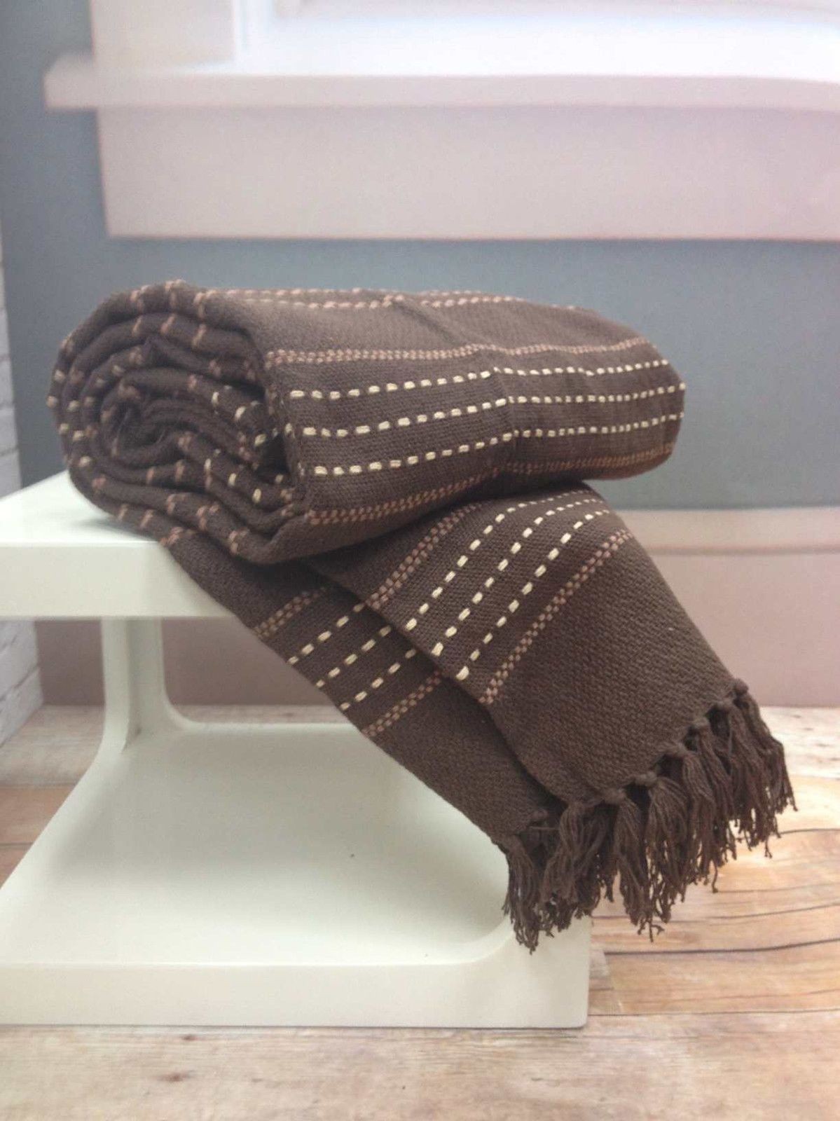 Stitch stripe throw in double chocolate brown, featuring a textured weave with contrasting lighter stripes and fringed edges, neatly rolled on a white display stand.