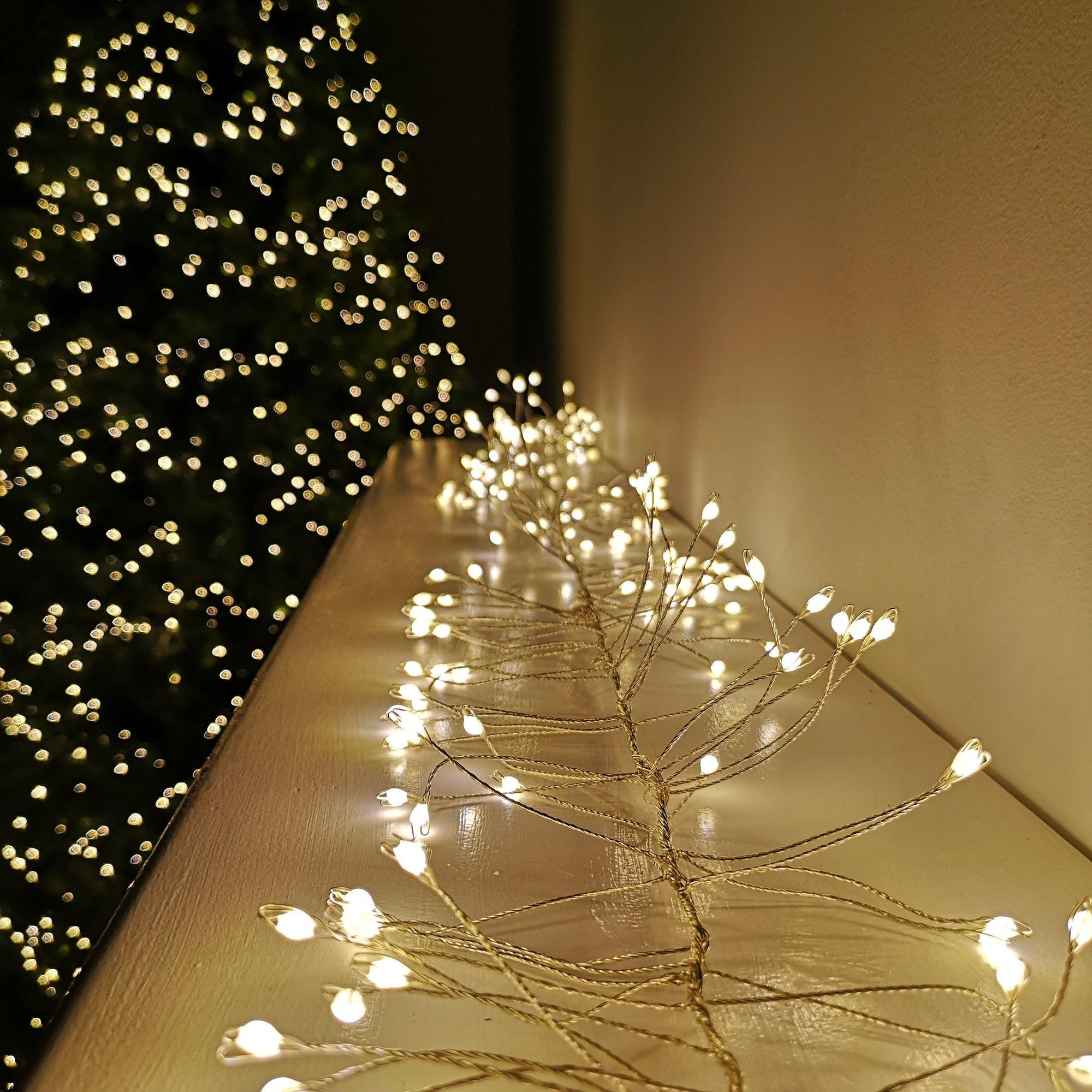 Warm white LED garland wire lights with 8 functions, featuring delicate branches and a 2.7m length, set against a softly blurred Christmas tree backdrop.