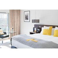 Hotel room with a large bed, yellow pillows, gray throw, modern decor, window view, and seating area with table.