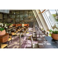 Modern dining area with wooden tables, chairs, large windows, and potted plants at Crowne Plaza Glasgow.