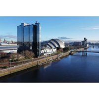 Crowne Plaza Glasgow by river, modern glass facade, near iconic dome-shaped building, clear blue sky.
