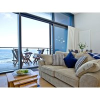 Coastal apartment with beige sofa, striped cushions, glass doors opening to balcony with ocean view and outdoor seating.