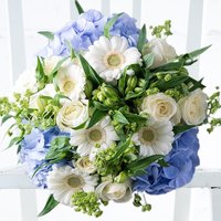 Bouquet of white roses, daisies, and green buds with blue hydrangeas, arranged in a lush, rounded display.