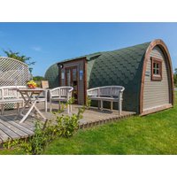 Curved wooden cabin with green shingle roof, brown door, and deck with white outdoor furniture.
