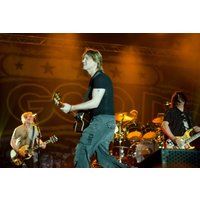 Band performing on stage with guitars and drums, under warm stage lights, backdrop displaying "Goo Goo Dolls".