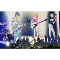 Animated Gorillaz band members on stage backdrop with live musicians, featuring colorful characters and instruments.