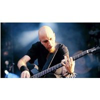 Bald musician playing a black electric bass guitar on stage with a focused expression and dramatic lighting.