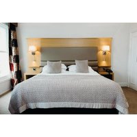Hotel room with a large bed, two pillows, wooden headboard, bedside lamps, and patterned curtains.