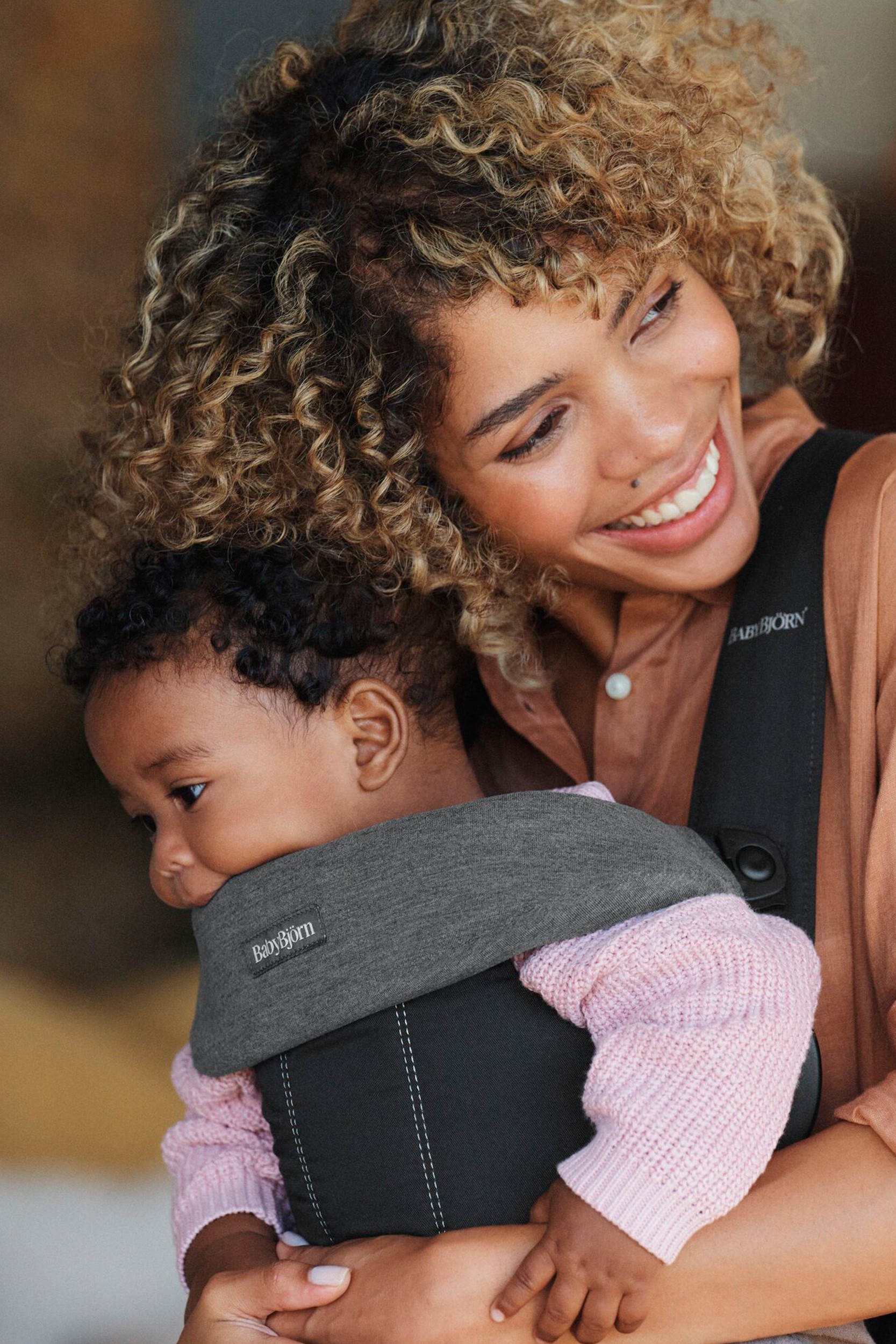 Dark grey jersey bib designed for BabyBjorn Mini and Move carriers, featuring soft fabric and a snug fit, worn by a smiling mother holding her baby.