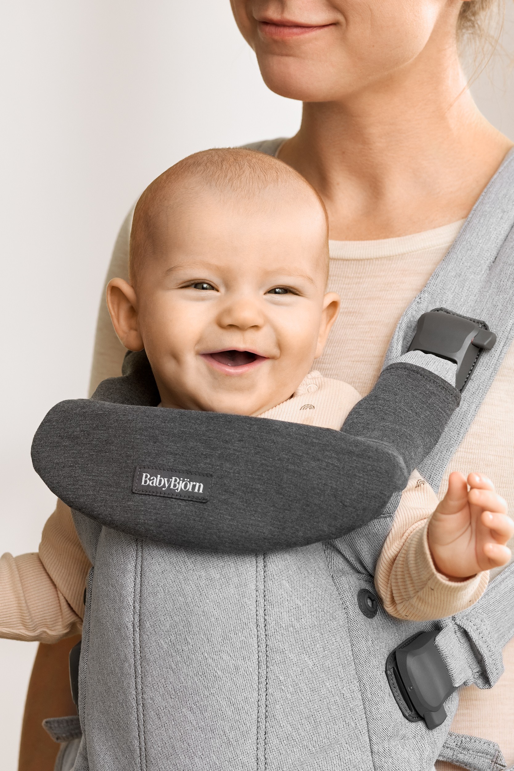 Dark grey bib for BabyBjorn Harmony baby carrier, made of soft fabric, featuring a logo patch, designed for comfort and protection while carrying a smiling baby.
