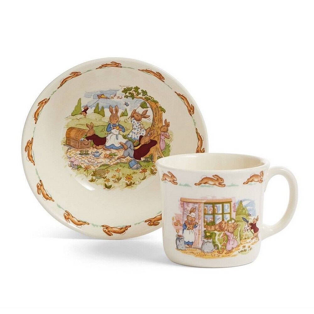 Ceramic infant bowl and mug set featuring colorful Bunnykins illustrations, with a whimsical scene of rabbits and floral accents on a cream background.