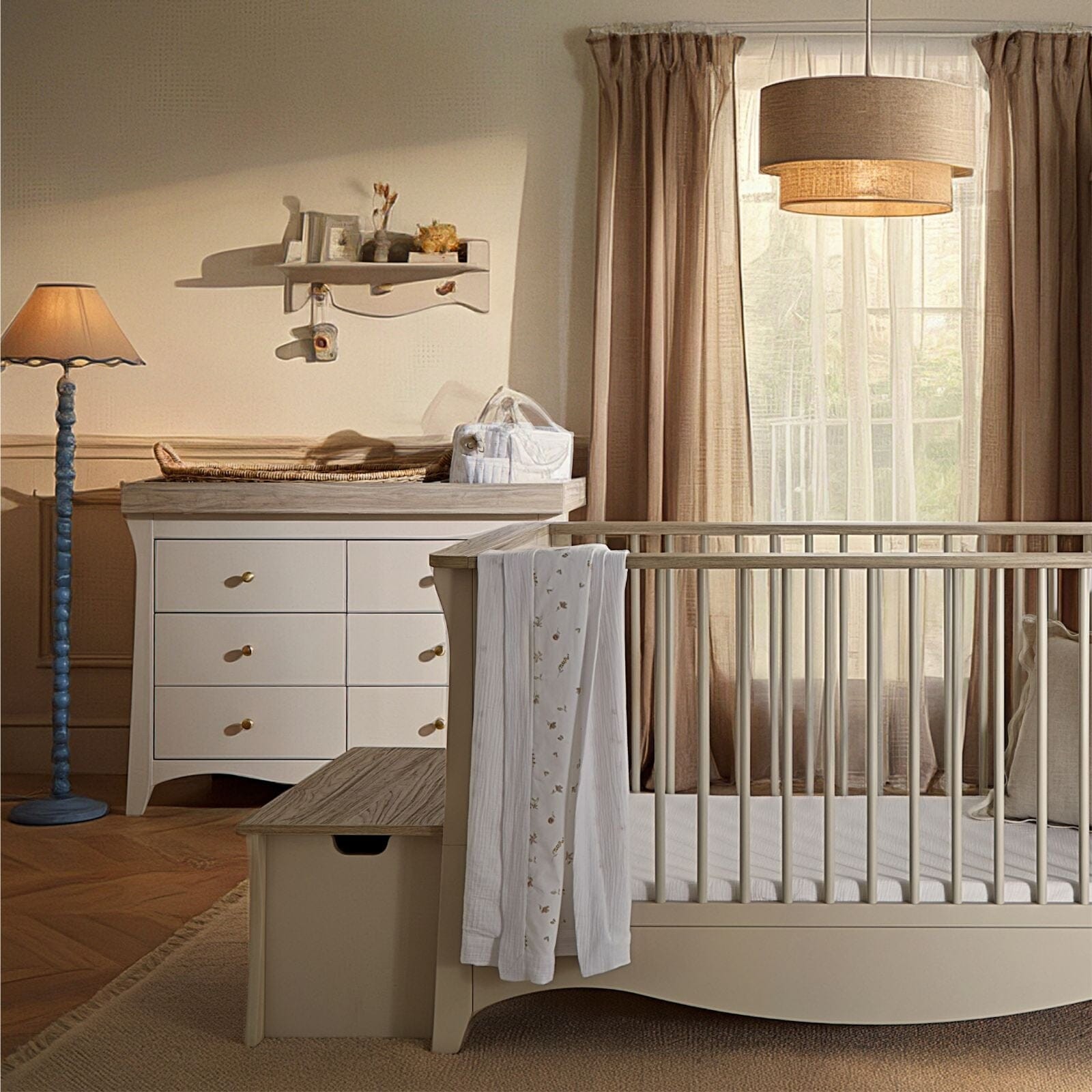Clara Luxe 2 Piece Furniture Set in cashmere and ash features a stylish crib with slatted sides and a matching dresser with gold handles, set in a softly lit nursery with neutral tones.