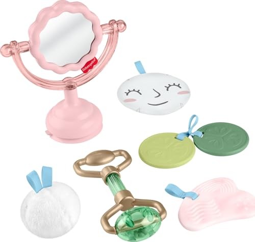 A pink tabletop mirror with a scalloped edge, a white facial disc with a smile, two green discs, a green rattle, and a fluffy white puff, all designed for sensory play.