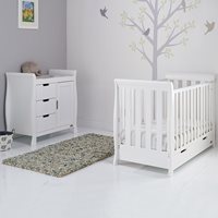 White wooden mini sleigh cot bed and matching dresser with two drawers, set against a light grey wall with a tree mural and a soft rug on a glossy floor.