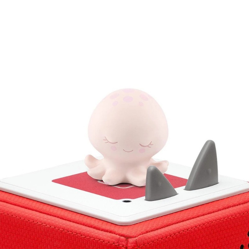 Soft pink octopus figurine with closed eyes and blush spots sits atop a red cube, featuring two gray fins, designed for bedtime storytelling.
