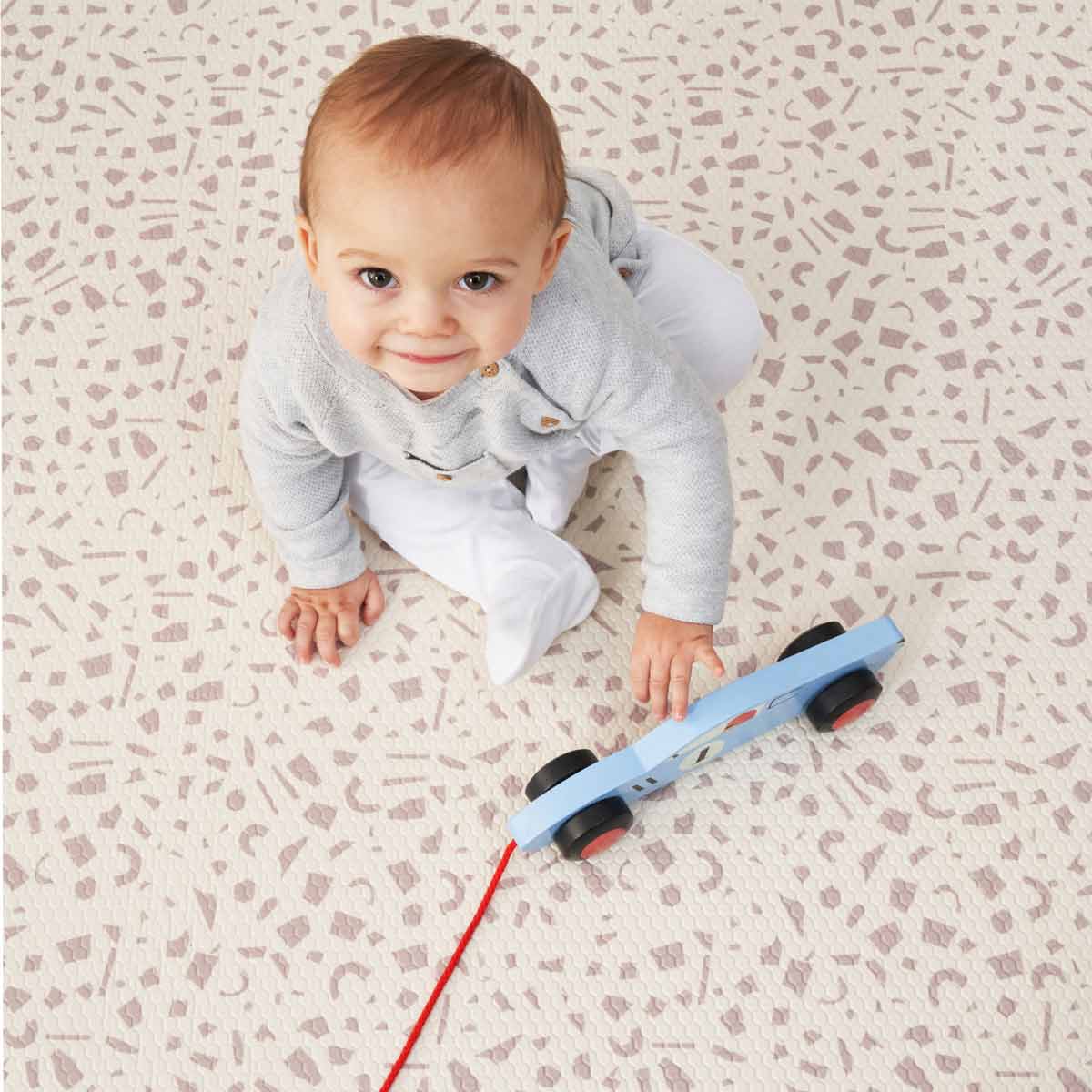 Luxury reversible playmat featuring a soft, cushioned surface in a bubble and terrazzo design, with a light color palette and a baby playing with a blue wooden toy car.