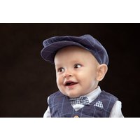 Baby in blue checkered outfit and cap, smiling against a dark background, part of "Bump to Baby Photoshoot" package.