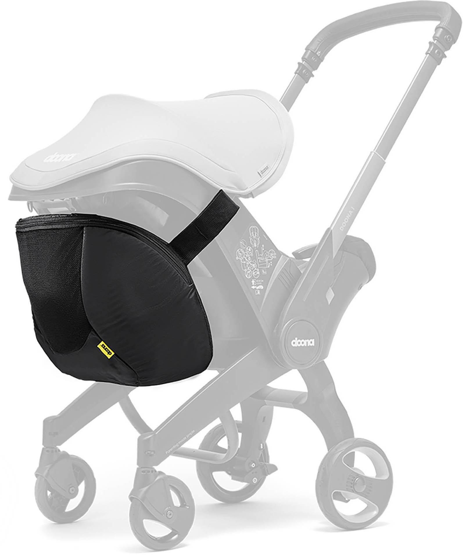 Black Doona Snap On Storage bag attached to stroller frame, featuring a sleek design with yellow logo tag.