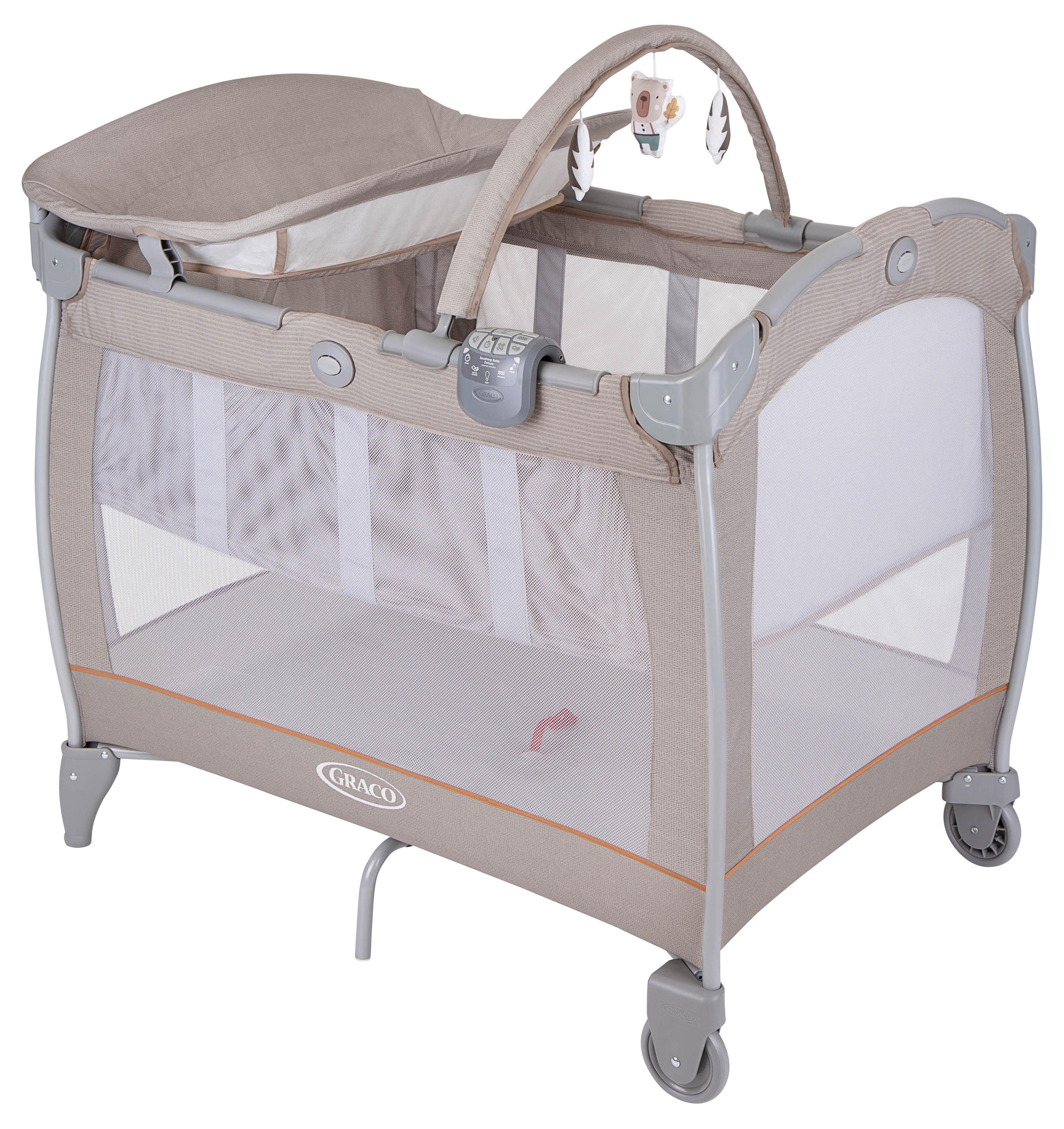 Beige Graco travel cot with bassinet, mesh sides, toy bar, and wheels, featuring "Little Adventures" design.