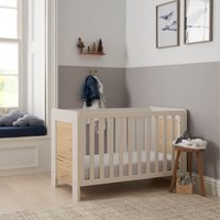 White sand and distressed oak mini cot bed with slatted sides and solid headboard, in a cozy nursery setting.