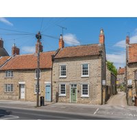 Stone cottage with red-tiled roof, green door, and two chimneys, part of a row of similar houses under a blue sky.