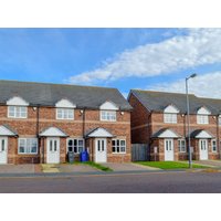 Red-brick semi-detached cottages with white doors, gabled roofs, and small front gardens under a blue sky.
