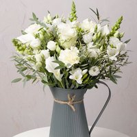 Bouquet of white roses and lisianthus in a gray ribbed metal jug with twine bow.