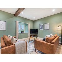 Cozy living room with two brown leather sofas, green walls, wooden beam, TV, and window with countryside view.